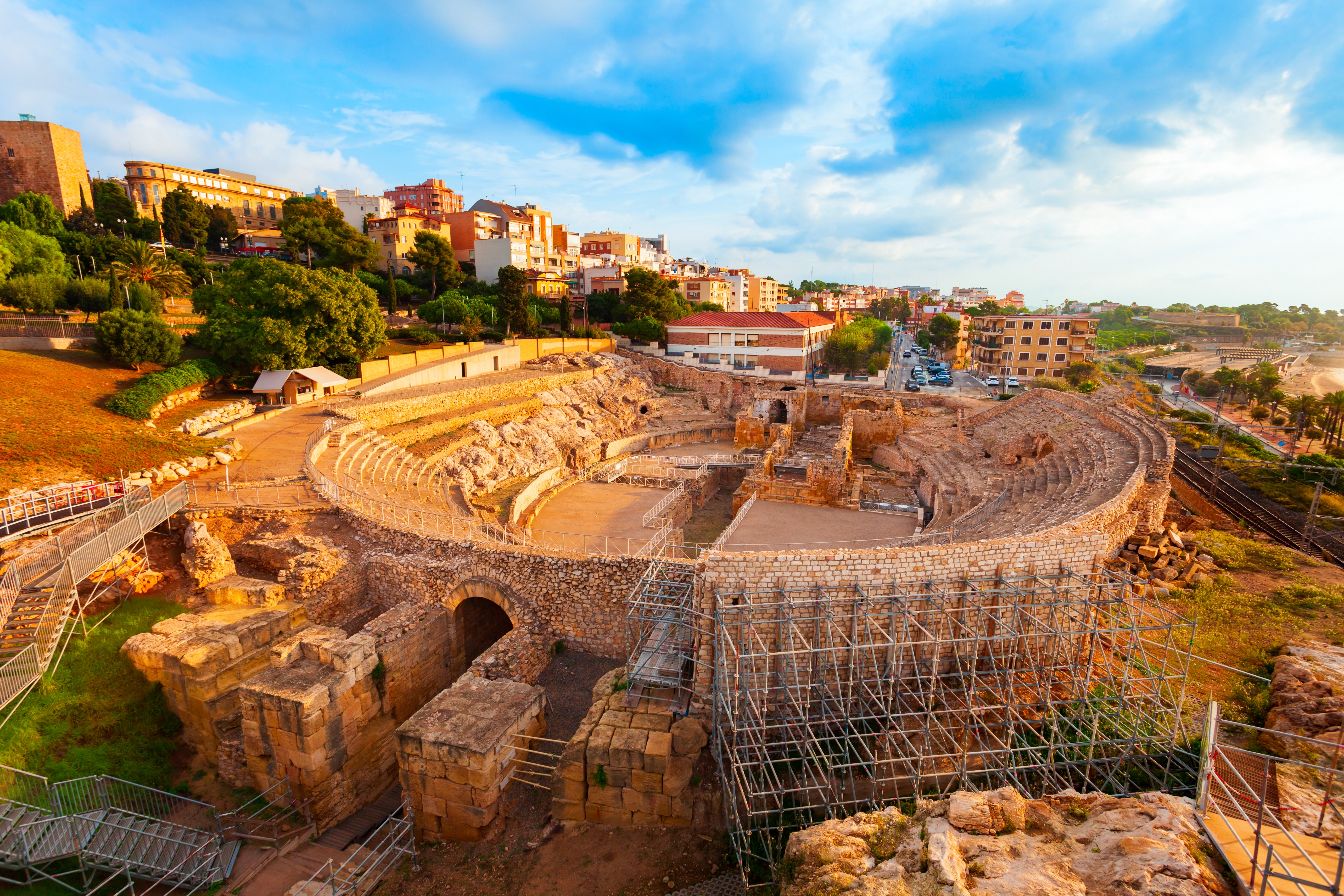Antikt romersk amfiteater i Tarragona Spanien med moderne bybygninger i baggrunden under gyldent lys