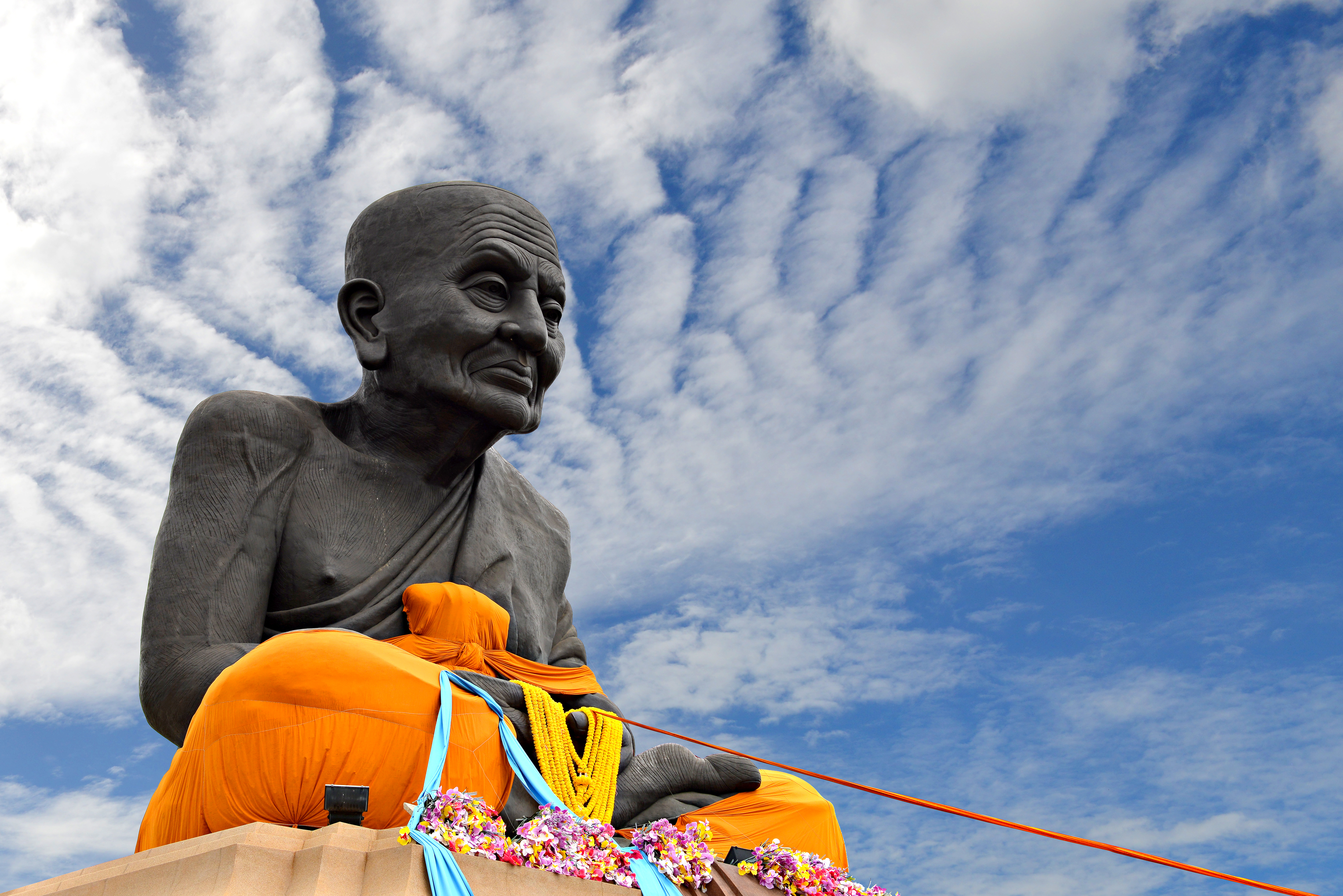 Buddhistisk statue med orange klæder mod blå himmel i Thailand