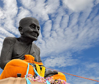 Buddhistisk statue med orange klæder mod blå himmel i Thailand