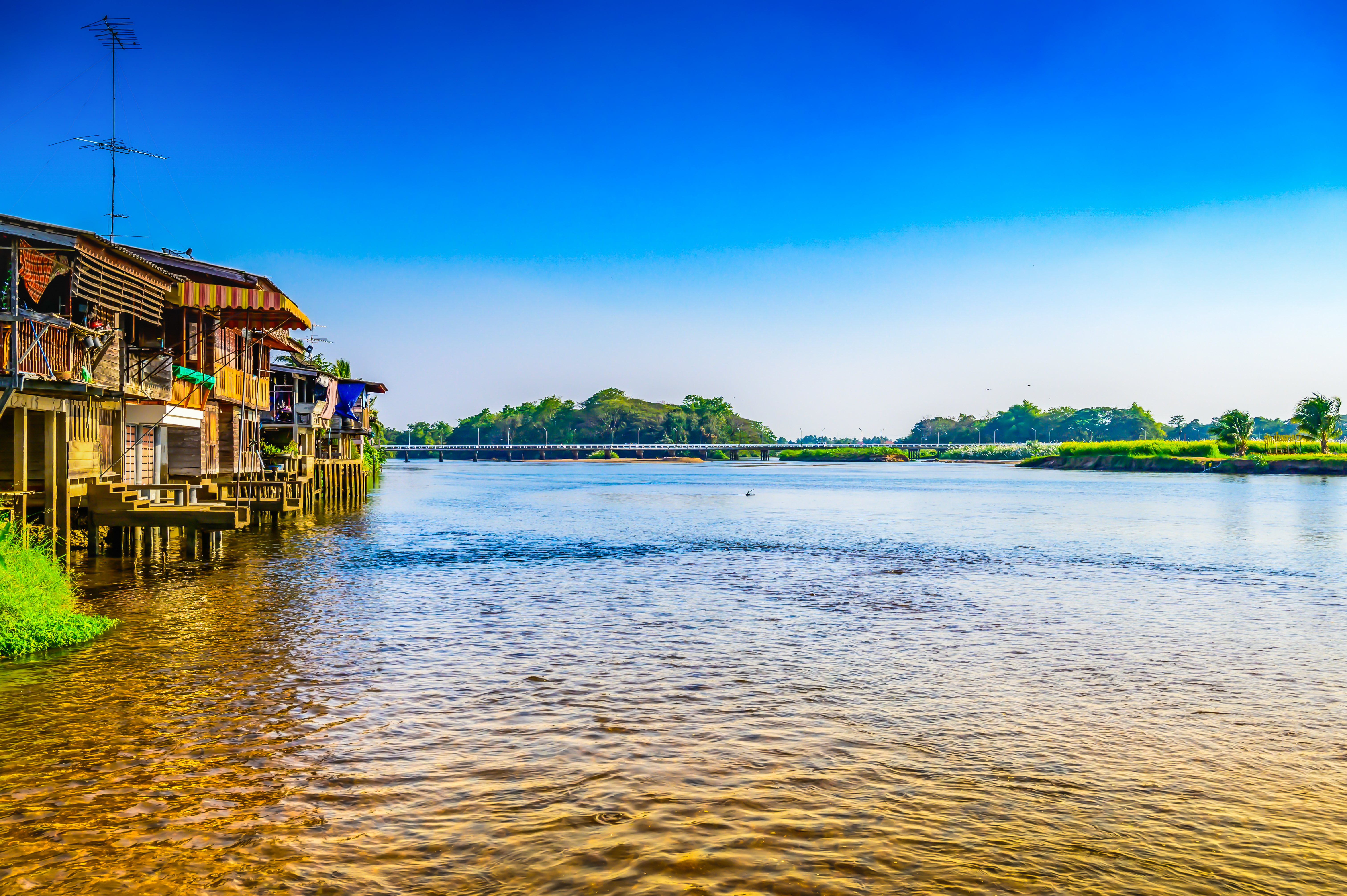 Traditionelle træhuse på stylter over Ping-floden i det nordlige Thailand med smuk natur og blå himmel