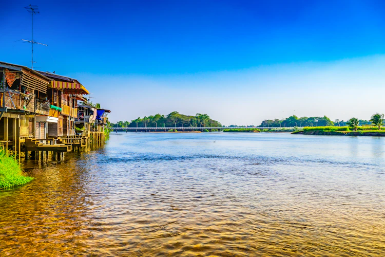 Traditionelle træhuse på stylter over Ping-floden i det nordlige Thailand med smuk natur og blå himmel