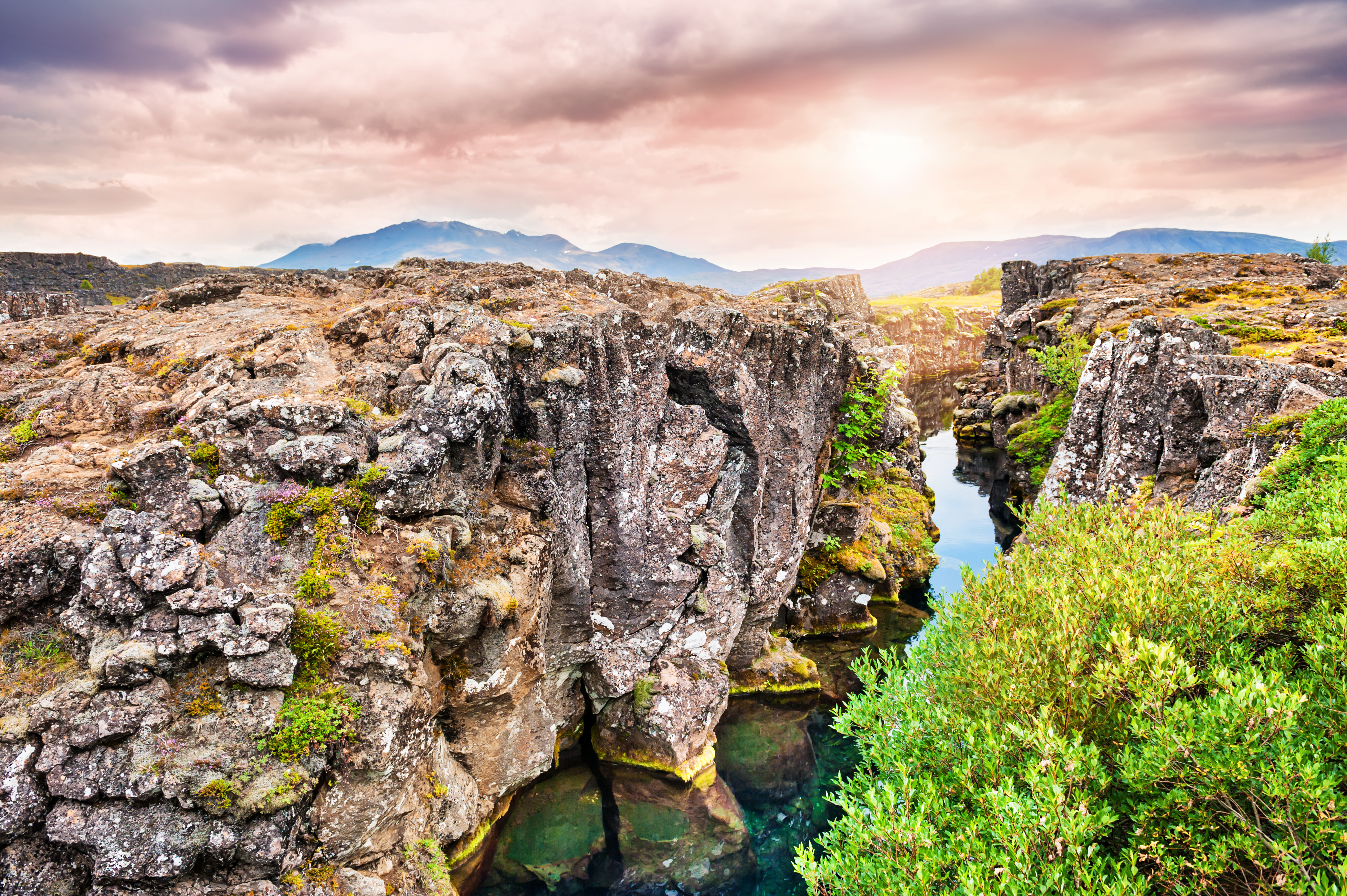 Thingvellir Nationalpark på Island med dramatisk riftspælte, turkisblåt vand og vulkanske klippeformationer ved solnedgang