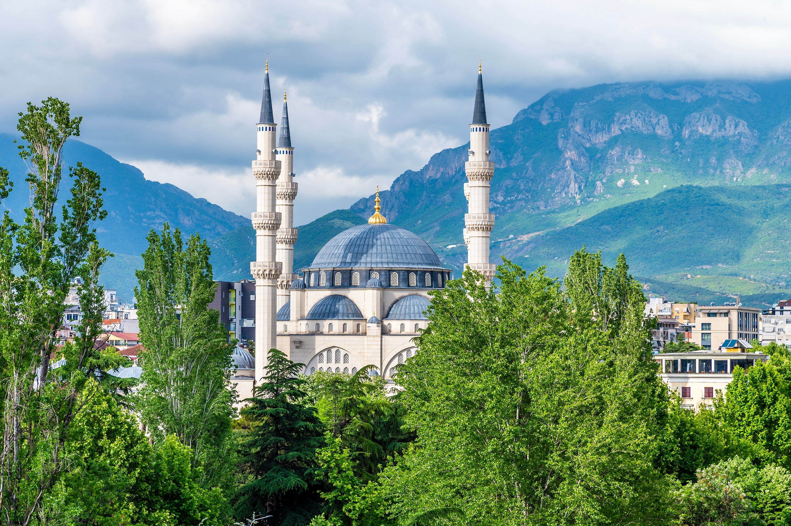 Sommerlig udsigt over det centrale Tirana med frodige grønne trætopppe og historiske moskéer, der rejser sig over Albaniens charmerende hovedstad