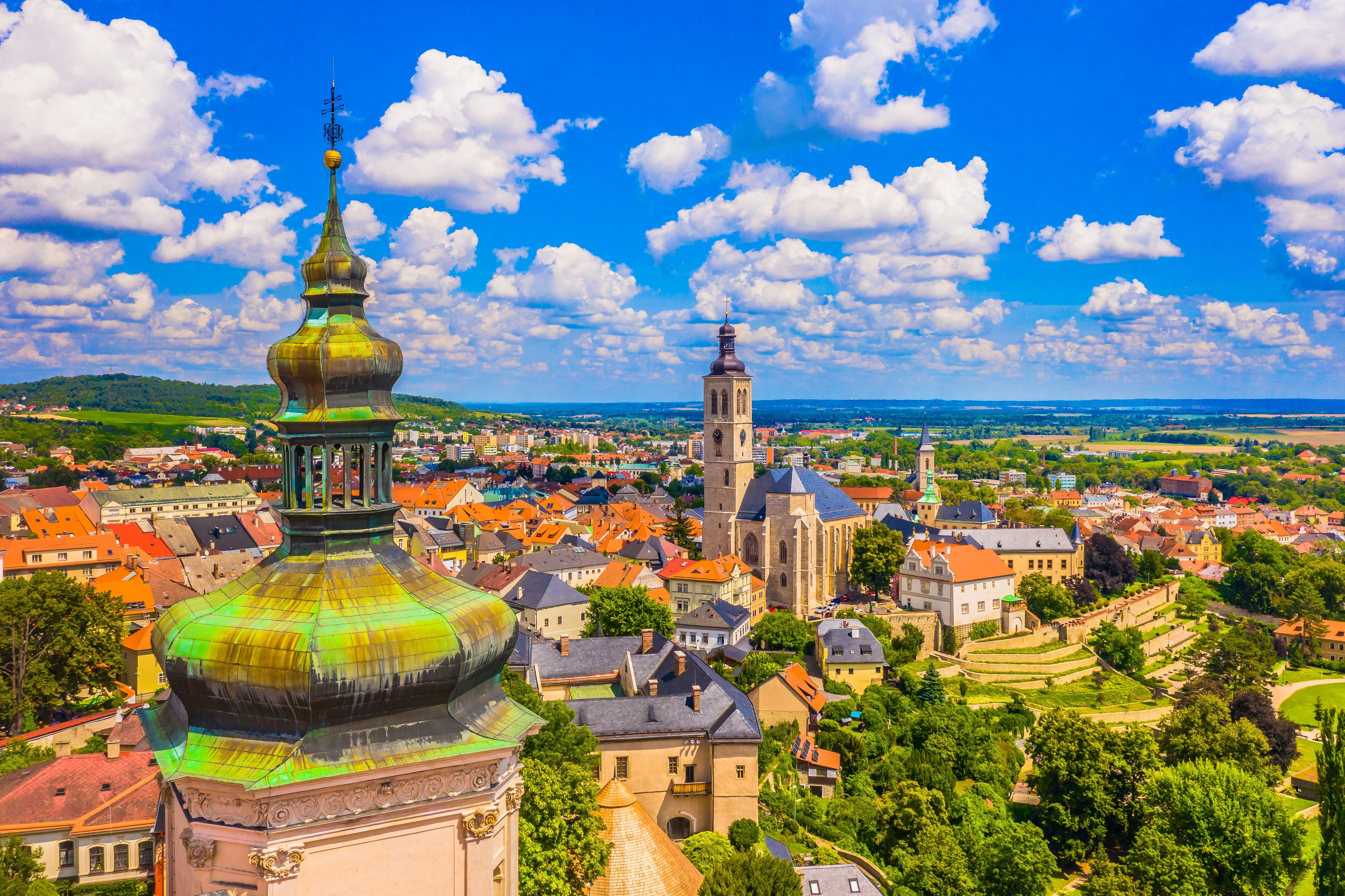 Luftfoto af historisk tjekkisk by med barok kirke og middelalderlige tårne under blå himmel