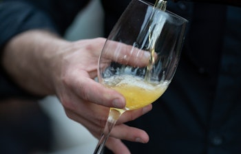 Tjener der skænker gylden cider i et vinglas ved udendørs restaurant, perfekt til gastronomiske rejseoplevelser