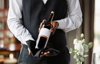 Professionel tjener præsenterer en flaske vin i en eksklusiv restaurant, perfekt til gourmetoplevelser på din rejse