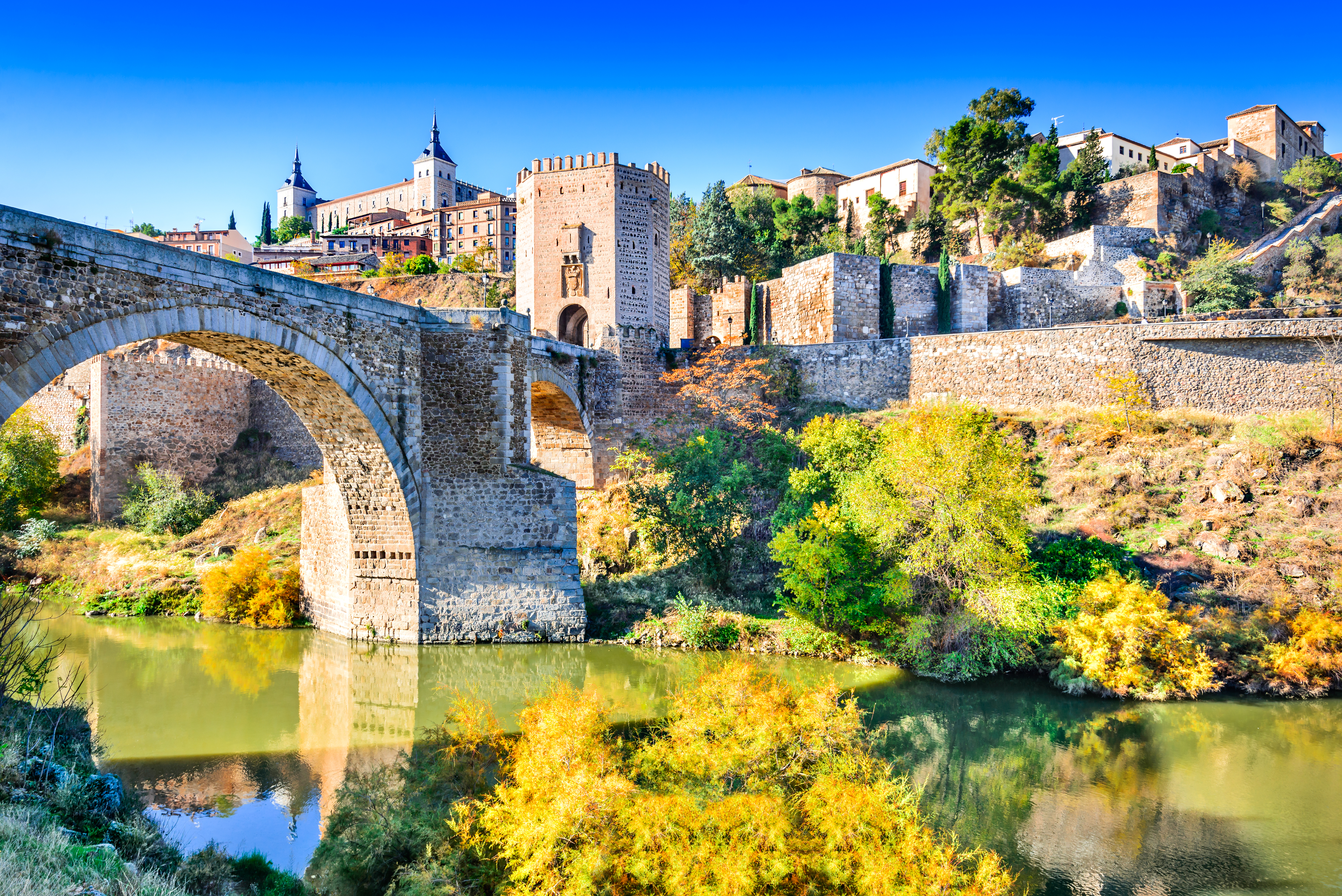 Historisk stenbro og middelalderborg i Toledo Spanien med efteraarsfarver ved Tagus floden