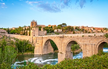 Historisk panoramaudsigt over Toledo i Spanien med gammel stenbro over den rolige flod og middelalderborg i baggrunden