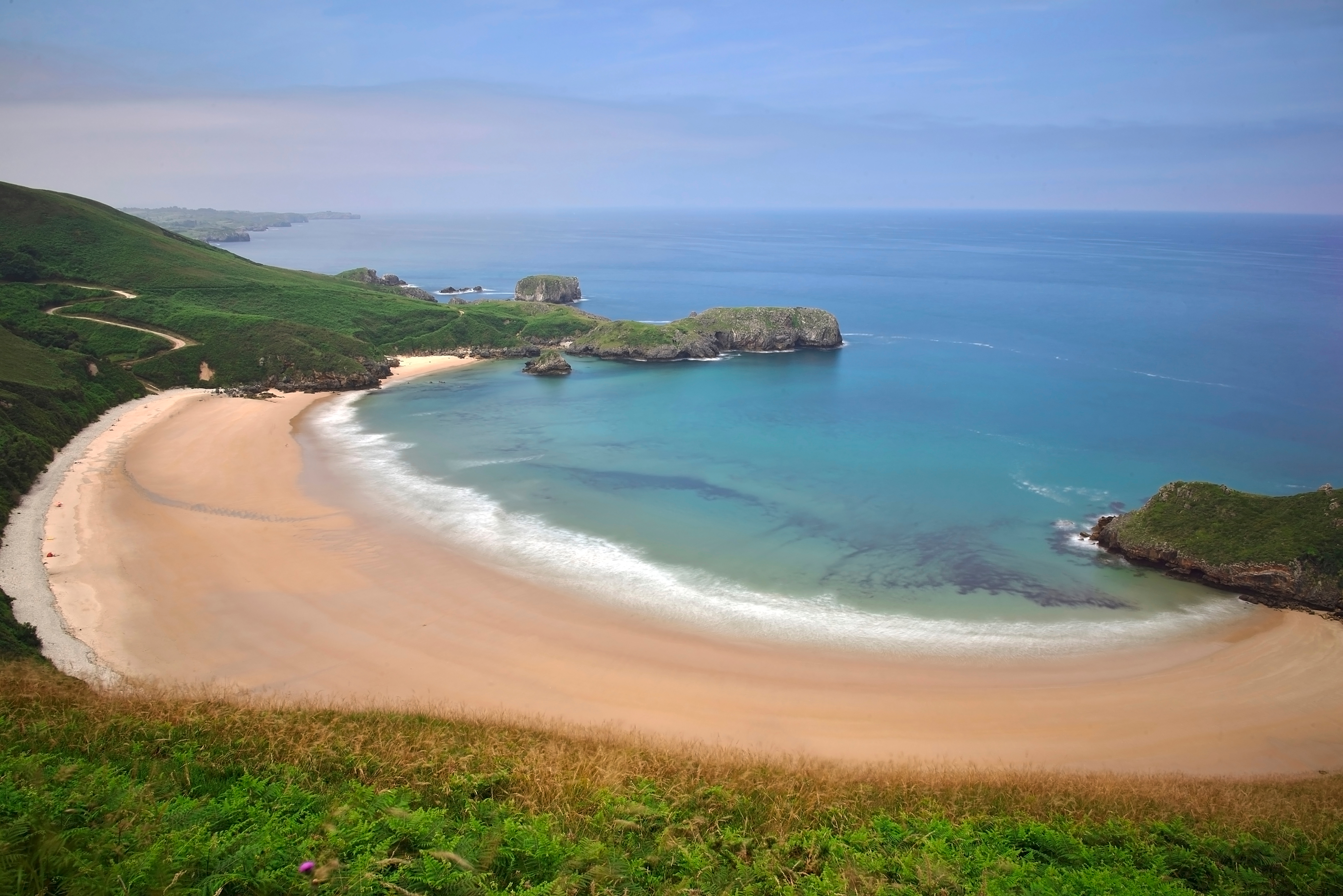Smuk udsigt over Torimbia stranden med krystalblåt vand og frodige grønne omgivelser i Llanes, Asturien, Spanien
