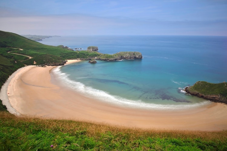 Smuk udsigt over Torimbia stranden med krystalblåt vand og frodige grønne omgivelser i Llanes, Asturien, Spanien