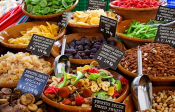 Farverige skåle med tørrede frugter og nødder på det traditionelle marked i Alcúdia på Mallorca, perfekt til en gastronomisk oplevelse under din rejse til Spanien.