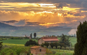 Idyllisk bondehus i Toscana med smukke bakker og landligt landskab ved solnedgang med gyldent lys over den italienske landsbygd
