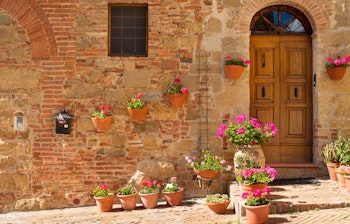 Charmerende gammel stenmur prydet med terrakottakrukker fyldt med farverige blomster i en idyllisk toscansk landsby i Italien