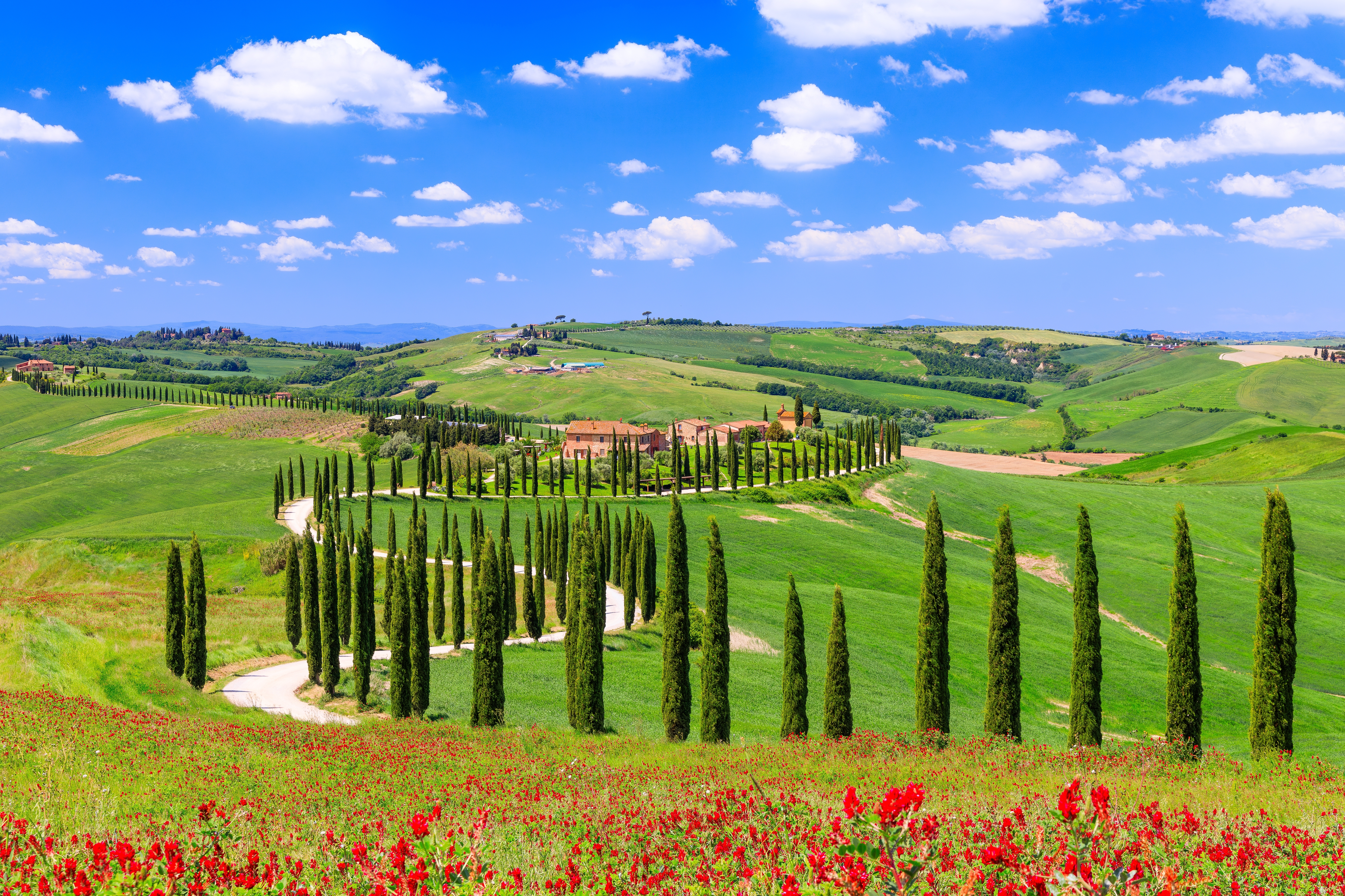 Idyllisk landskab i Val d'Orcia, Toscana med bølgende grønne bakker, cyprestræer, landhus og snoet grusvej under en smuk himmel