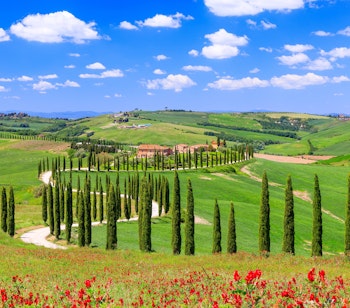 Idyllisk landskab i Val d'Orcia, Toscana med bølgende grønne bakker, cyprestræer, landhus og snoet grusvej under en smuk himmel