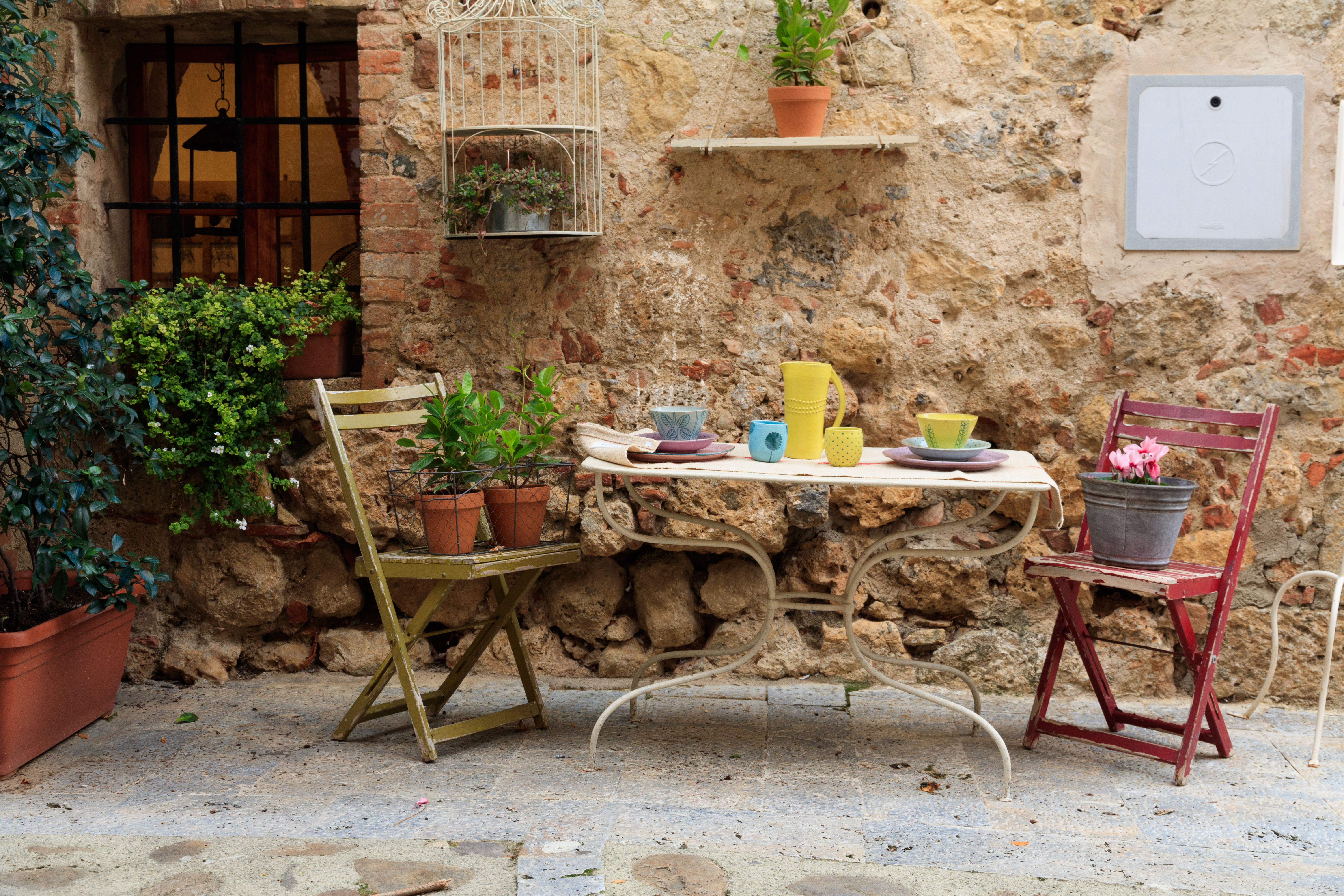 Charmerende udendørs cafe terrasse med farverige stole og stenmur i Toscana Italien
