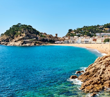 Betagende udsigt fra vandsiden af Vila Vella med de historiske fæstningsmure og middelalderlige bygninger i Tossa del Mar ved Costa Bravas azurblå Middelhav