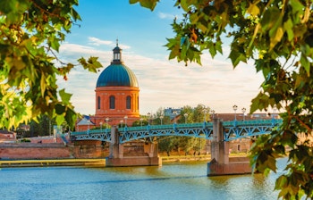Malerisk solnedgang over Toulouse med Garonne-floden i forgrunden og La Grave-kuppelen der rejser sig over den rosa bys historiske bygninger