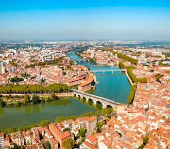 Luftpanorama over Toulouse og Garonne-floden med historiske bygninger, broer og blå himmel i Sydfrankrig