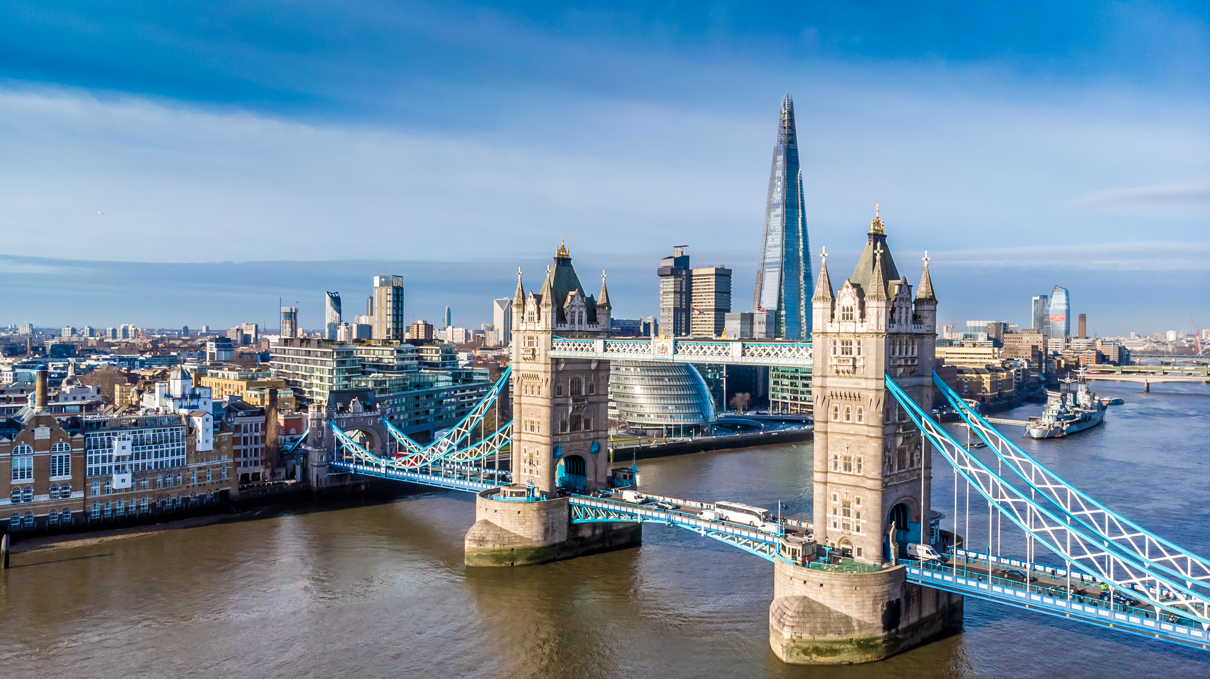Luftfoto af Tower Bridge over Themsen med The Shard og Londons skyline i baggrunden på en solrig dag