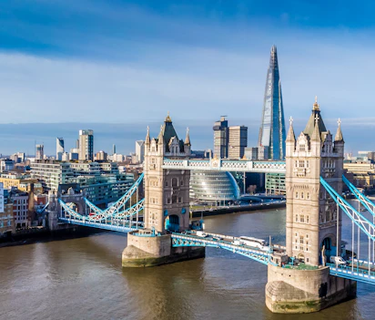 Luftfoto af Tower Bridge over Themsen med The Shard og Londons skyline i baggrunden på en solrig dag