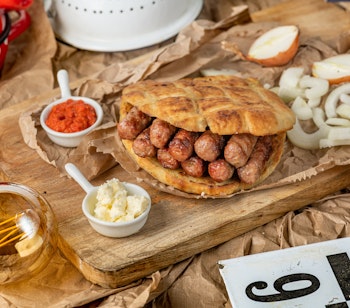 Traditionel balkanret cevapi med grillede kødpølser serveret med fladbrød, løg og rød pebersauce