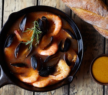 Traditionel bouillabaisse fra Marseille med rejer, muslinger og hummer serveret i kobberpande med sauce rouille på rustikt træbord - en ægte fransk kulinarisk oplevelse