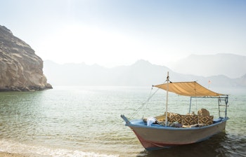 Traditionel dhow-båd sejler langs Musandams kyst i Oman med turkisblåt hav og dramatiske bjerge i baggrunden