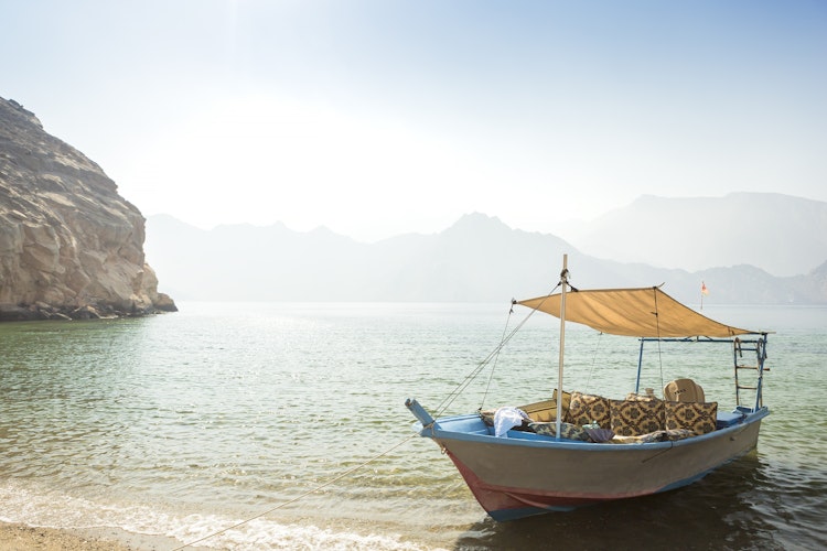 Traditionel dhow-båd sejler langs Musandams kyst i Oman med turkisblåt hav og dramatiske bjerge i baggrunden