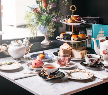 Elegant engelsk afternoon tea med sølvtepot, fine porcelænskopper, scones, sandwiches og kager serveret på marmorbord