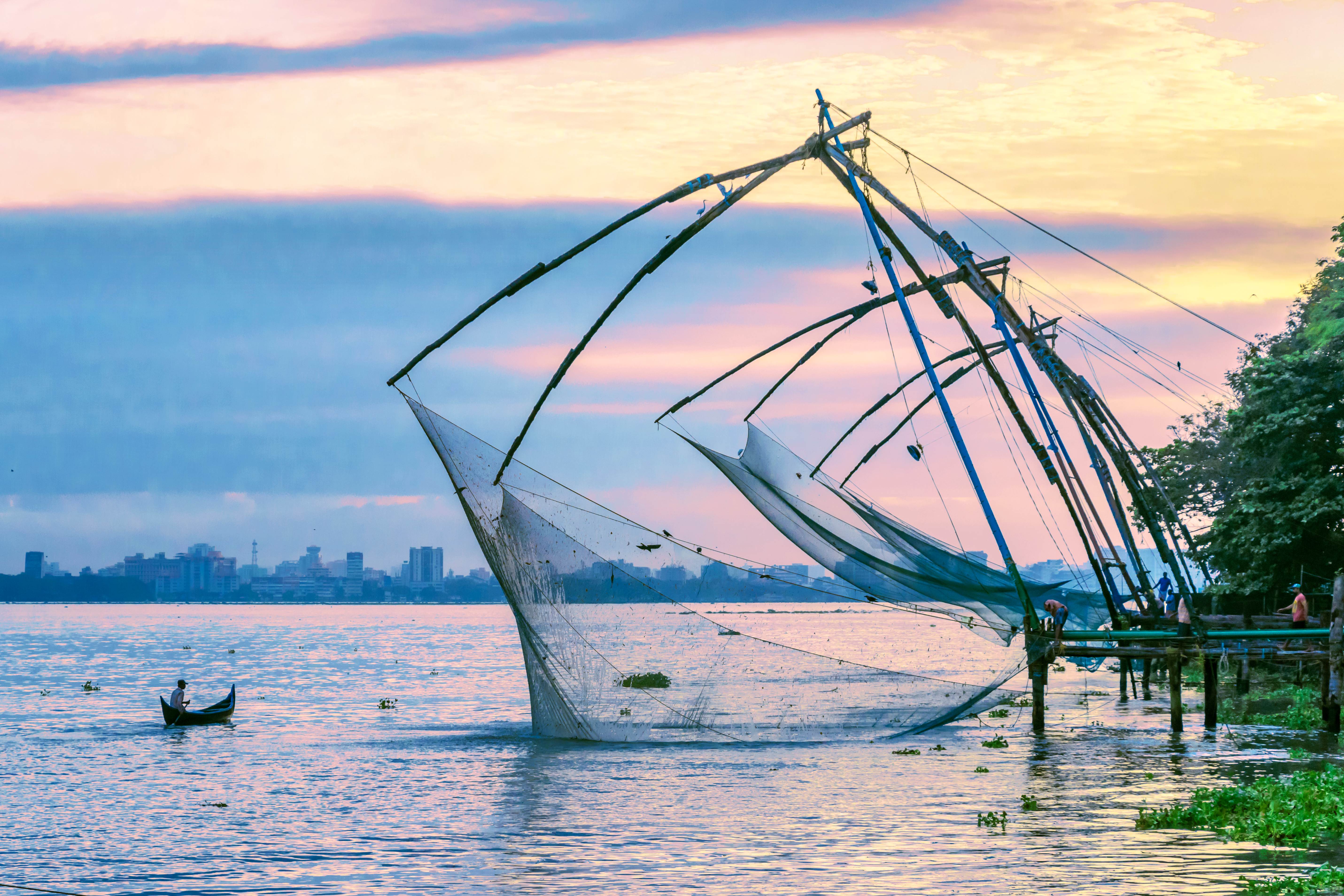 Silhuet af en traditionel fisker med net ved Fort Kochi-stranden i Kerala, Indien med en farverig solnedgang over Det Arabiske Hav