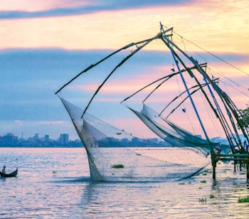 Silhuet af en traditionel fisker med net ved Fort Kochi-stranden i Kerala, Indien med en farverig solnedgang over Det Arabiske Hav