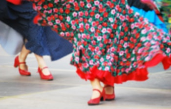 Traditionelle folkedansere i farverige blomstrede kjoler udfører kulturel dans med røde sko