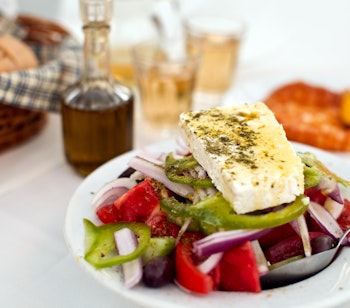 Autentisk græsk salat med feta, oliven og tomater serveret med hjemmebagt brød og lokal hvidvin på en hyggelig taverna i Mykonos, Grækenland