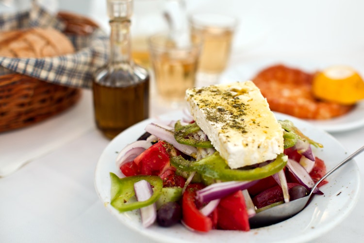 Autentisk græsk salat med feta, oliven og tomater serveret med hjemmebagt brød og lokal hvidvin på en hyggelig taverna i Mykonos, Grækenland