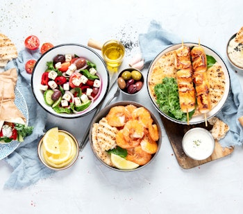 Autentisk græsk madbuffet med meze, souvlaki, tzatziki, feta, oliven og andre traditionelle middelhavslækkerier på grå baggrund