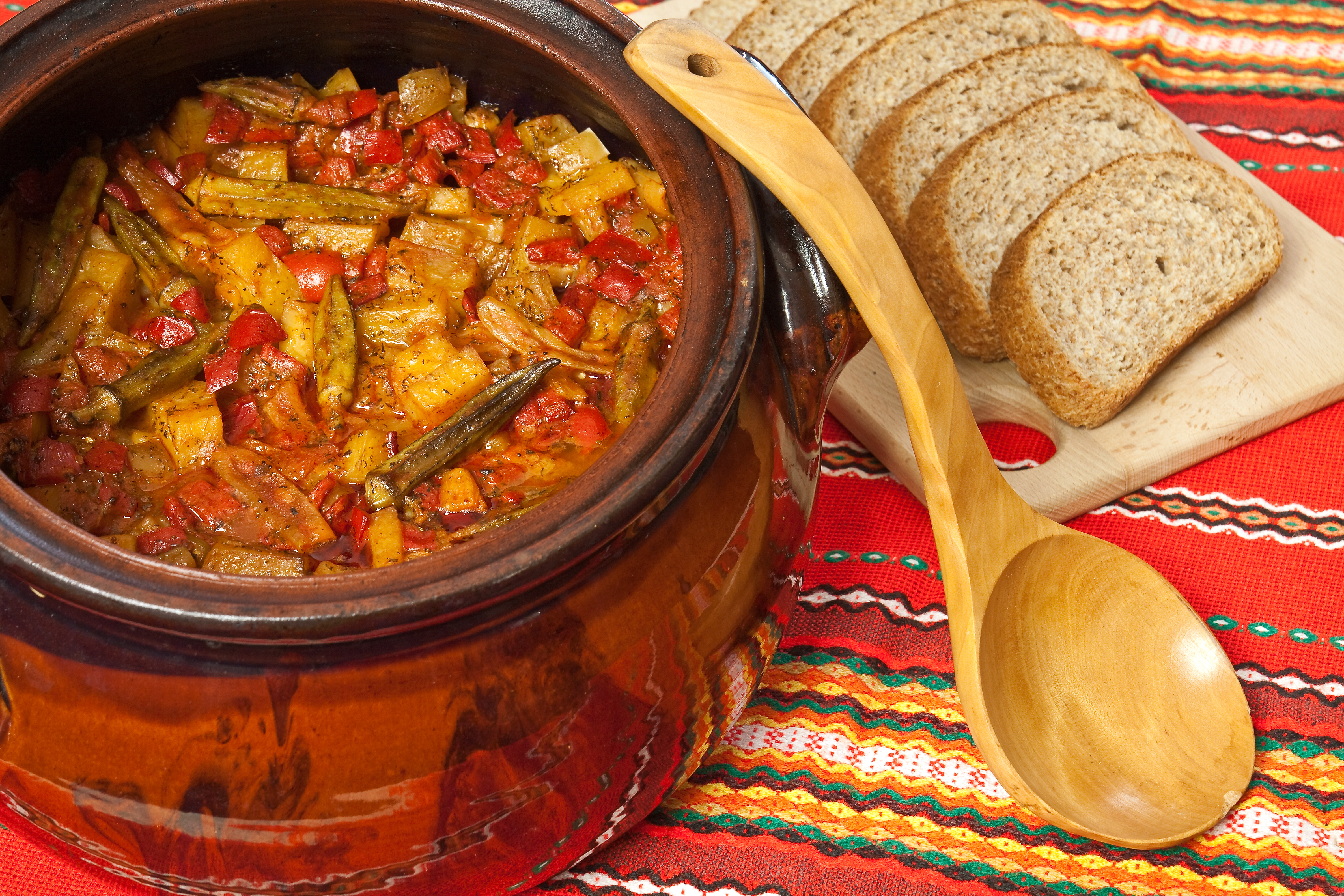 Traditionel grøntsagsgryde med okra og tomater serveret i lerpotte med rustikt brød