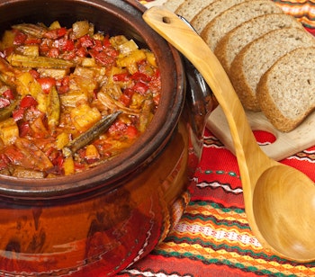 Traditionel grøntsagsgryde med okra og tomater serveret i lerpotte med rustikt brød