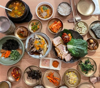 Traditionel koreansk madoplevelse med soyasauce-marineret krabbe og Bossam svinekøds-wraps serveret med sideanretninger på træbord