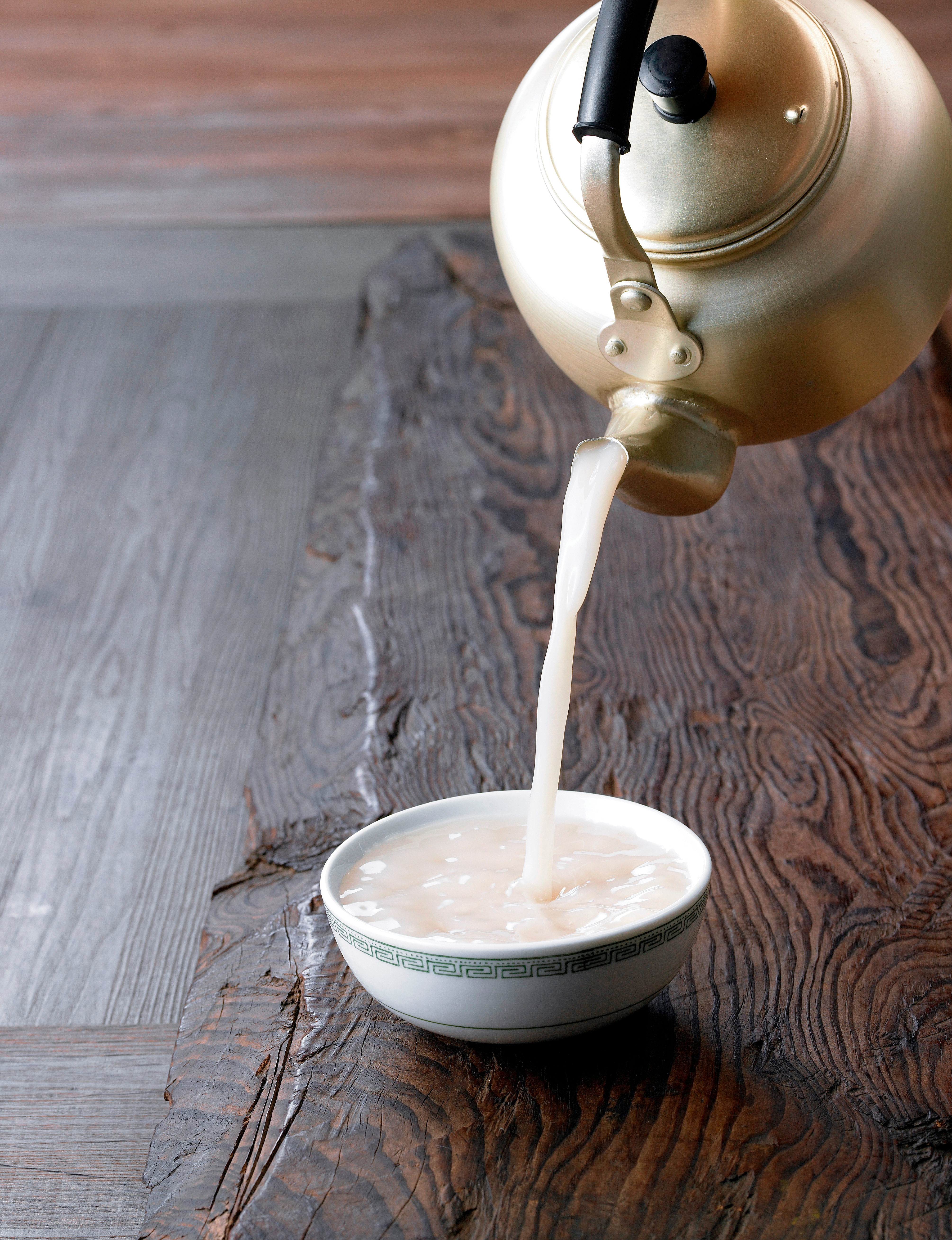 Traditionel koreansk risvin Makgeolli serveret i træskål på rustikt bord, en populær mælkeagtig alkoholisk drik i Korea