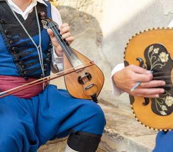 Traditionelle musikere i farverige folkedragter spiller kretensisk lyra og lut ved kulturel optræden på Kreta