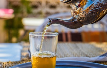 Traditionel marokkansk mint te hældes fra en dekorativ kande på en tagterrasse i Marrakech, en autentisk smagsoplevelse på rejsen