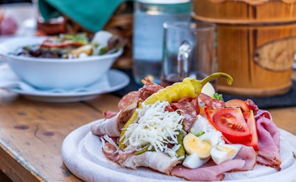 Traditionel østrigsk Brettljause anretning med pålæg, ost og brød serveret med juice på et træbord i Steiermark
