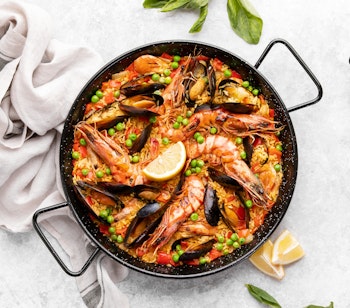 Traditionel spansk paella med skaldyr, rejer og muslinger i autentisk paellapande, serveret med friske citronskiver
