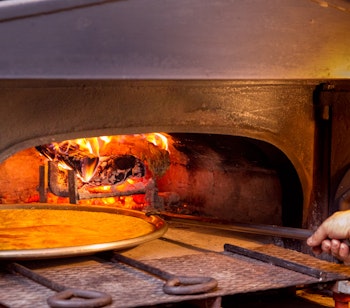 Traditionel træfyret stenovn i Genova hvor en kok tilbereder farinata, en lokal italiensk specialitet lavet af kikærtemel