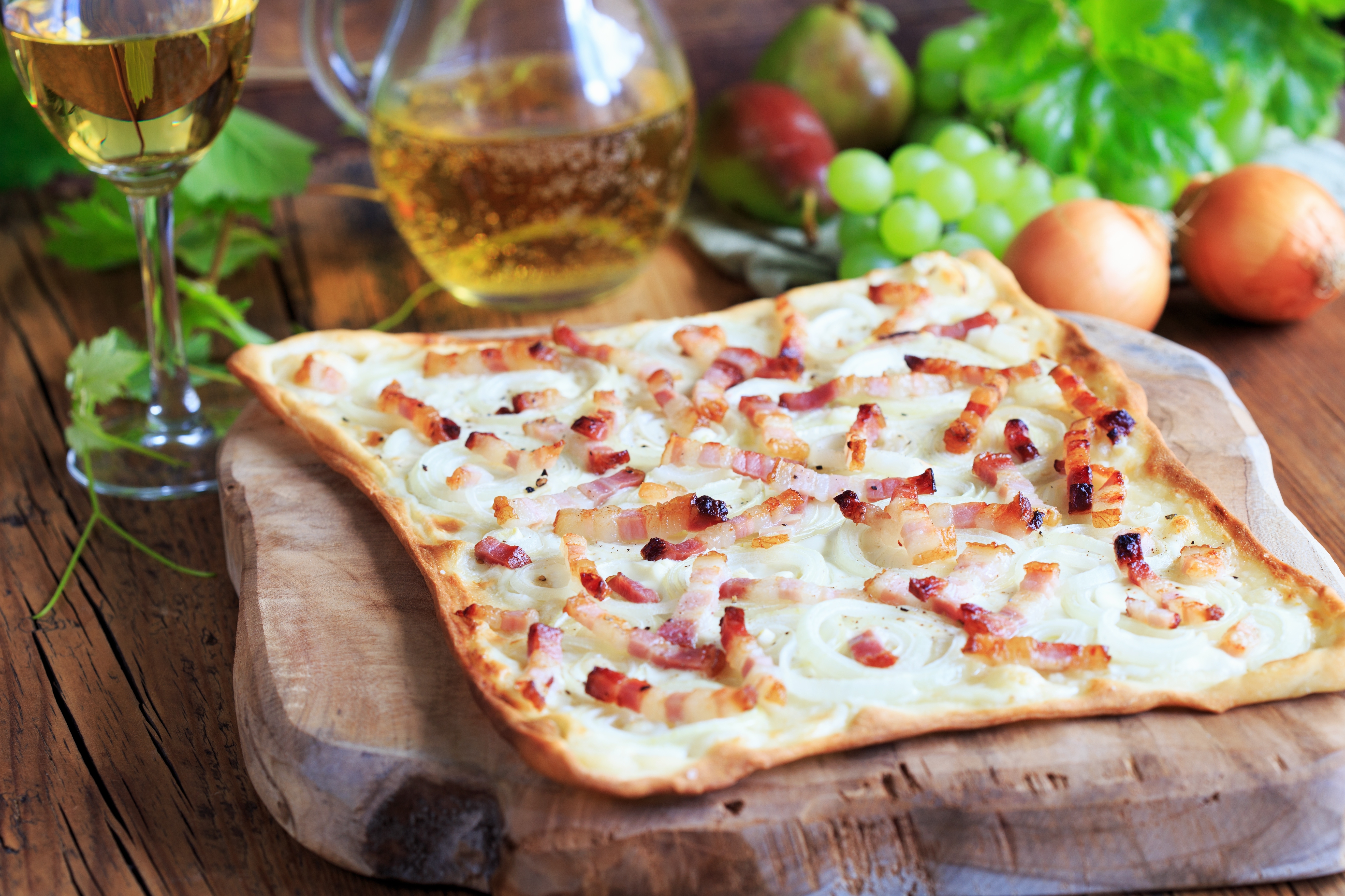 Traditionel tarte flambée fra Alsace med bacon og løg serveret på træbræt med hvidvin, en lokal fransk specialitet
