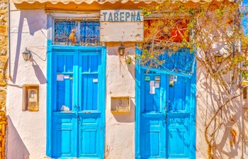 Charmerende hvid taverna med blå døre og vinduer på Hydra-øen i Grækenland, perfekt eksempel på traditionel græsk arkitektur