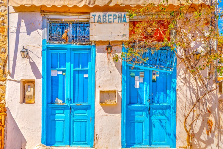 Charmerende hvid taverna med blå døre og vinduer på Hydra-øen i Grækenland, perfekt eksempel på traditionel græsk arkitektur