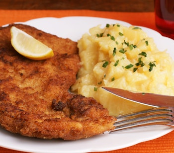 Klassisk Wiener Schnitzel serveret med kartoffelsalat og friske purløg, en østrigsk specialitet