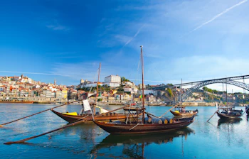 Traditionelle træbåde med portvinsfade på Douro-floden med Porto's historiske bylandskab og bro i baggrunden